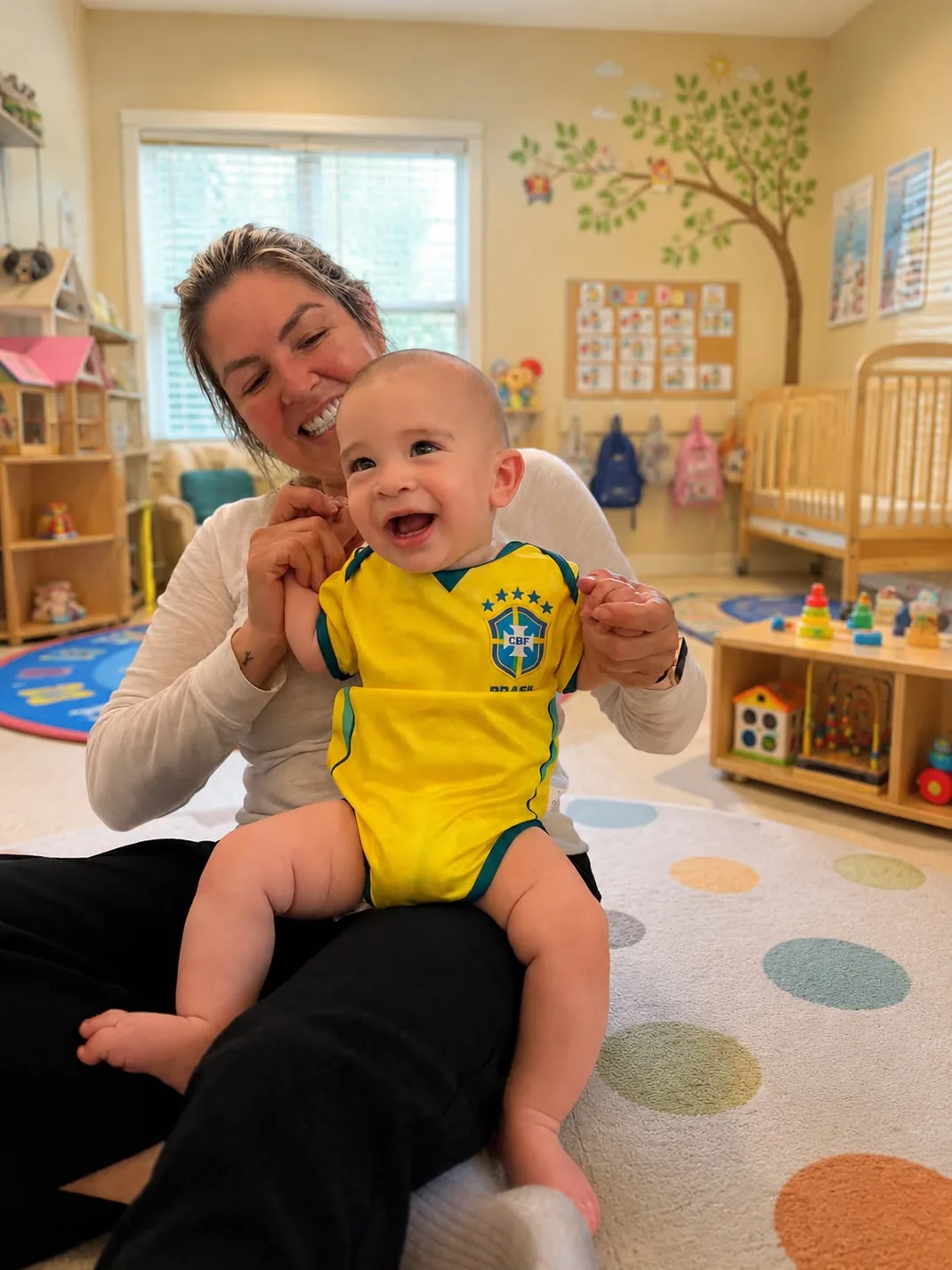 Flávia holding a happy smiling baby in the playroom
